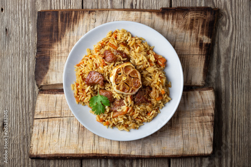 Oriental cuisine. Uzbek pilaf or plov from rice and meat. Wooden rustic background. Top view vith copy space.