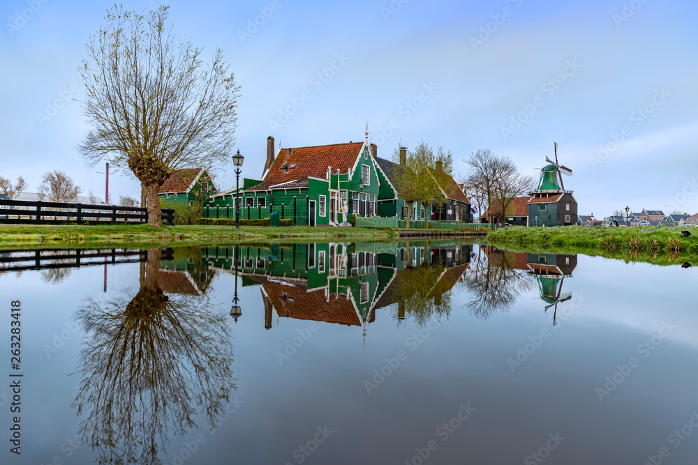Long exposure of a reflection of the wooden green houses topped with dark orange color roof reflected on the calm water of the canal