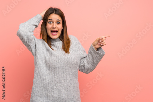 Young woman over pink wall surprised and pointing finger to the side