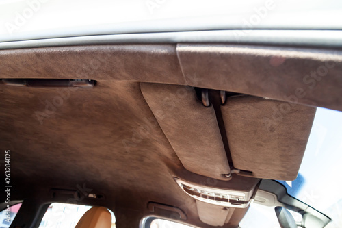 The ceiling of the SUV car pulled by brown soft material alkantara in the workshop for tuning and styling the interior, view from the passanger opened door on central mirror and sun visorson the roof photo