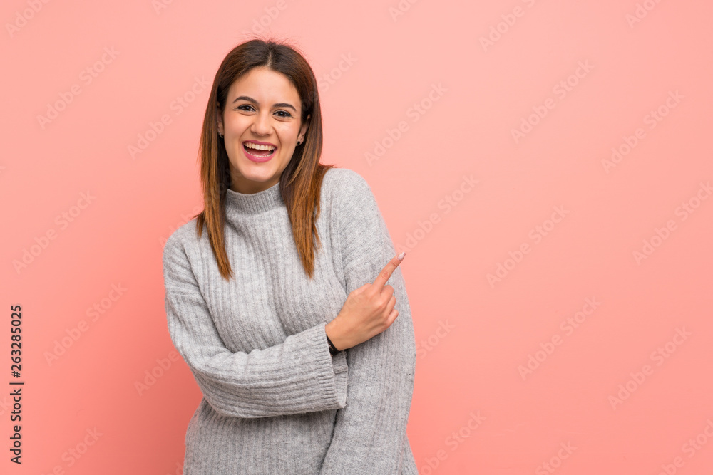 Young woman over pink wall pointing to the side to present a product Young woman over pink wall pointing to the side to present a product