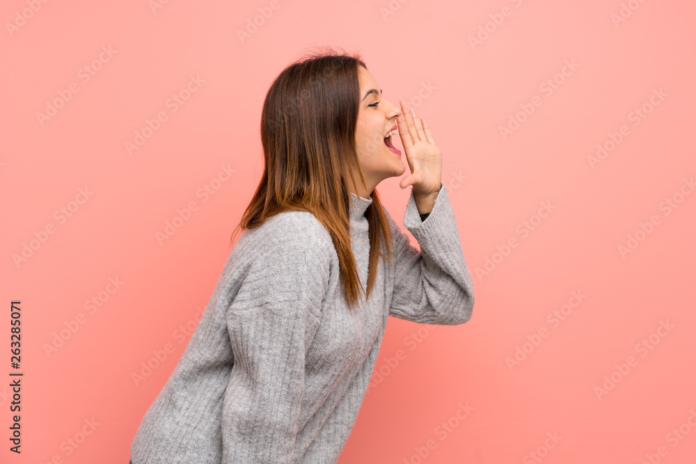 Young woman over pink wall shouting with mouth wide open to the lateral Young woman over pink wall shouting with mouth wide open to the lateral