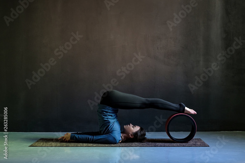 Girl in halasana pose doing yoga on black background. photo