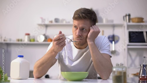 Upset single man eating tasteless cereals for breakfast, lack of appetite