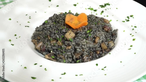 Traditional mediterranean black risotto - rice with seafood on a traditional Mediterranean plate garnished with summer vegetables and fruits - greece, croatia, italy, montenegro, squid.