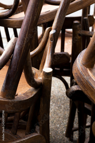 Stacked wooden dining chairs stored outside a restaurant with shallow depth of field 