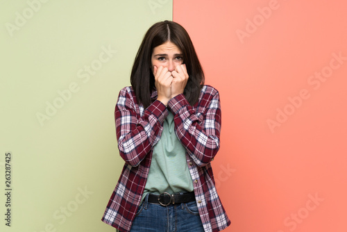 Young woman over isolated colorful wall nervous and scared putting hands to mouth © luismolinero