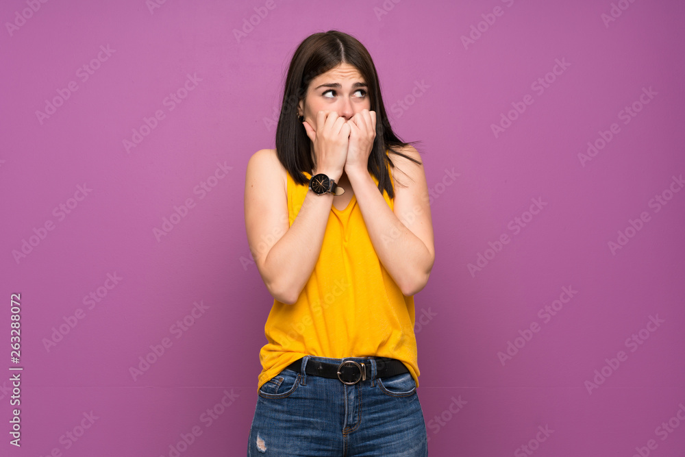 Young woman over isolated purple wall nervous and scared putting hands to mouth Young woman over isolated purple wall nervous and scared putting hands to mouth