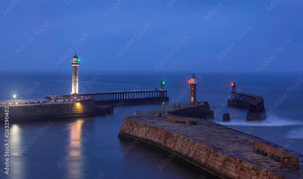Blue twilight in Whitby. Lighthouses on the East and West Piers. North Yorkshire. North Sea. England. UK. Long exposure. Main focus on piers