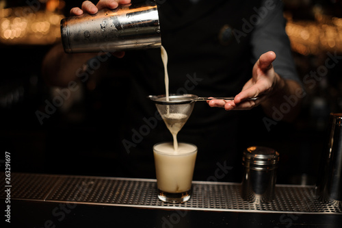 Close-up of bartender pouring cocktail using sieve and shaker
