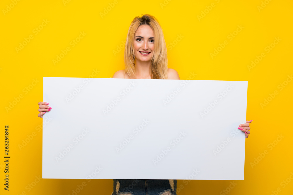 Young blonde woman over isolated yellow wall holding an empty white placard for insert a concept Young blonde woman over isolated yellow wall holding an empty white placard for insert a concept
