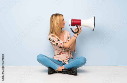 Young blonde woman sitting on the floor shouting through a megaphone