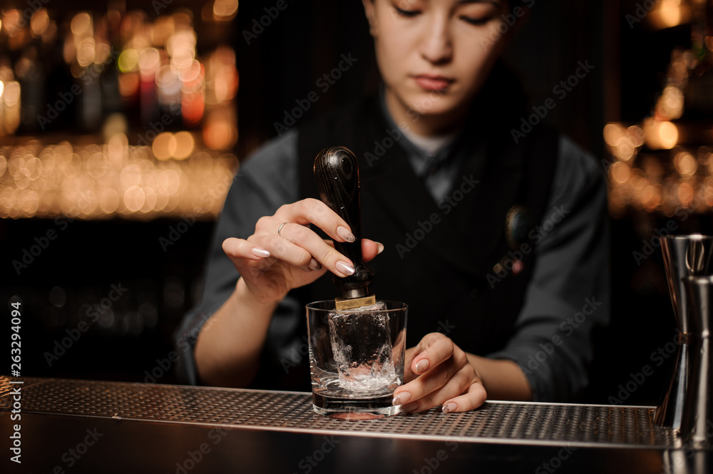 Bartender adds ice in glass with an ice picker