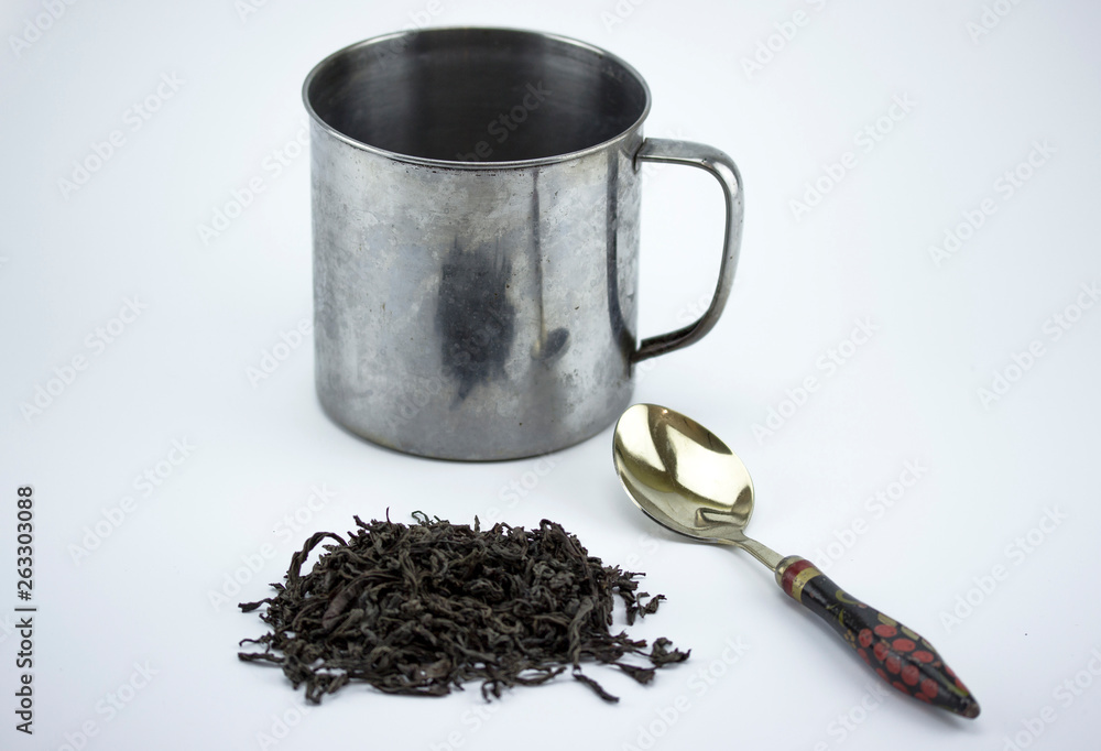 An old metal mug, a spoon with a wooden painted handle. Russian dishes, make some tea. isolated on white background. An old metal mug, a spoon with a wooden painted handle. Russian dishes, make some tea. isolated on white background.