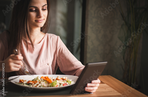 Young woman having lunch and reading electronic book at the restaurant