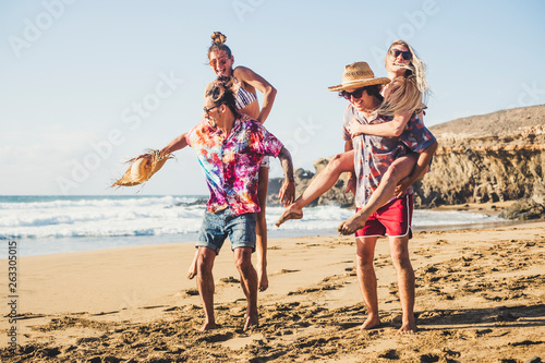 Happy group of people on vaation - youthful and funny concept with young men and women having fun together in friendship playing - boys carrying girls on their back - laugh and smile