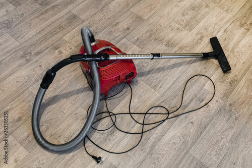 Red vacuum cleaner with electric cable laid out on the linoleum floor