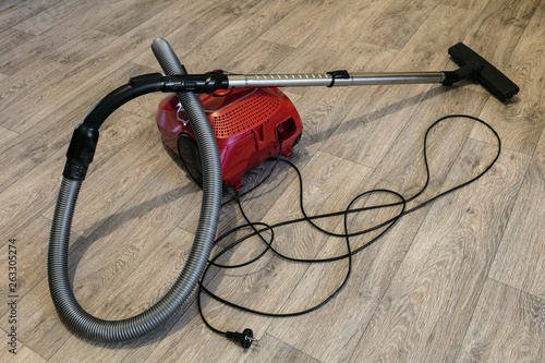 Red vacuum cleaner with electric cable laid out on the linoleum floor