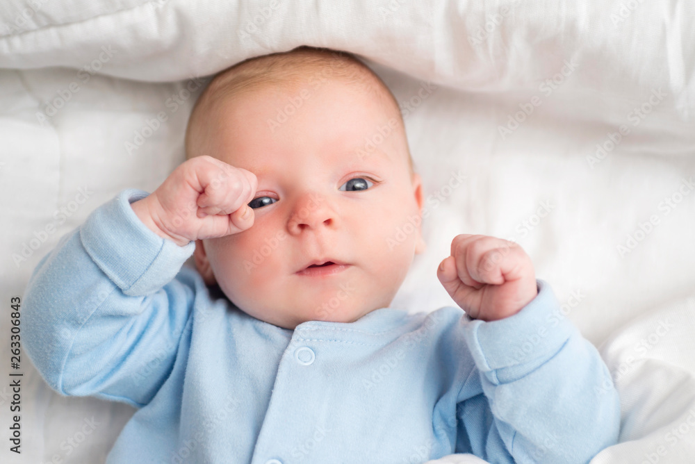 Baby lying down on back, happy toddler in bodysuit looking up. Portrait of a cute baby lying down on a bed, top view Baby lying down on back, happy toddler in bodysuit looking up. Portrait of a cute baby lying down on a bed, top view
