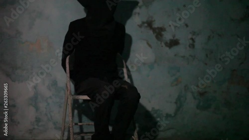 Male human wearing a black colored mask and black attire tied hands and sitting on the metal chair. Kidd napping concept. photo