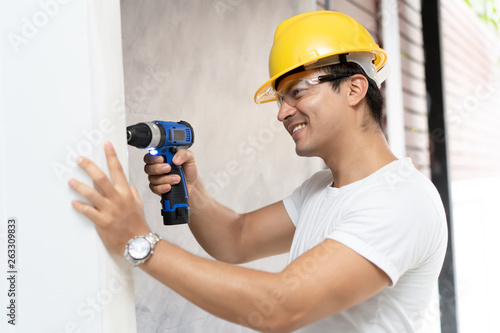 Man in helmet with electric drill making hole in wall Architecture and Home renovation concept.