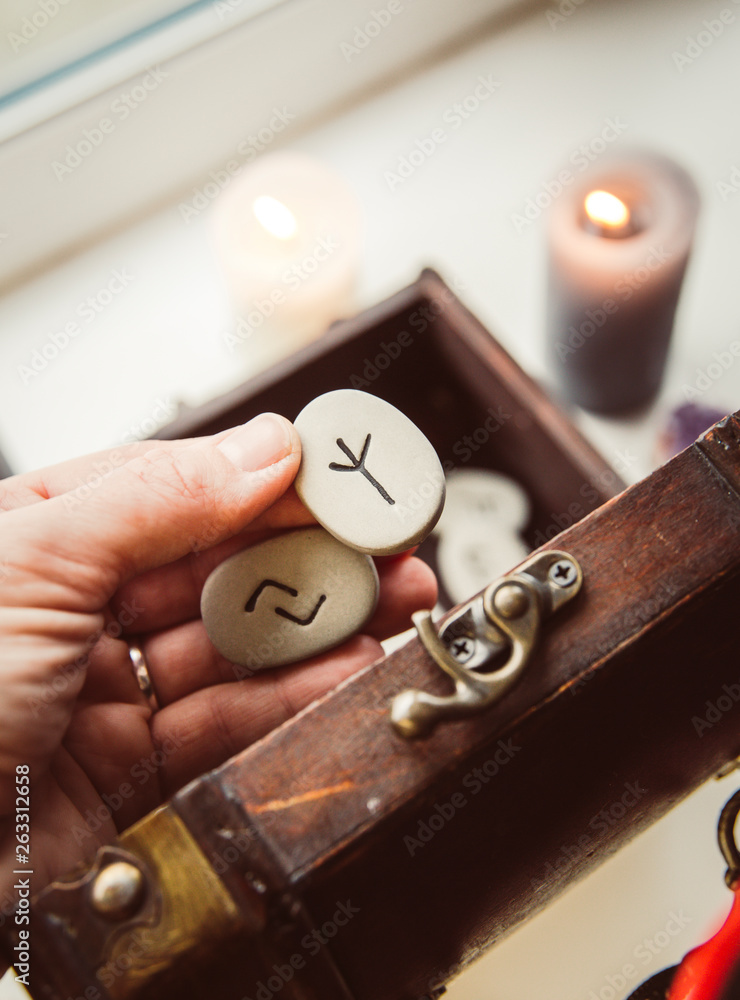 Hand holding rune stones, taking out of the wooden box container, self-prophecy concept. Candles burning. Hand holding rune stones, taking out of the wooden box container, self-prophecy concept. Candles burning.