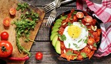mexican breakfast Chilaquiles.  tortilla chips are lightly stewed in a red tomato and paprika chili sauce, scrambled eggs are added and served in a pan with avocado and green onions and cilantro. 