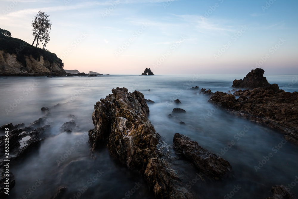 Long exposure fluffy ocean mists rush over tidal pool rocks at the beach