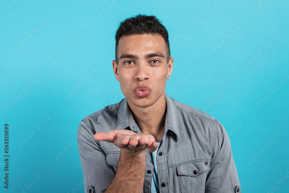 Pretty Man sending an air kissis and looks at the camera against a blue background Pretty Man sending an air kissis and looks at the camera against a blue background