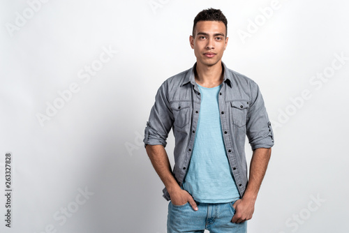 Studio shoot of a handsome man against the white wall, holding his hands in pockets