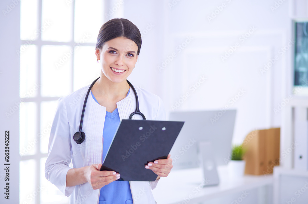 Young smiling female doctor with stethoscope holding a folder at a hospital's consulting room Young smiling female doctor with stethoscope holding a folder at a hospital's consulting room