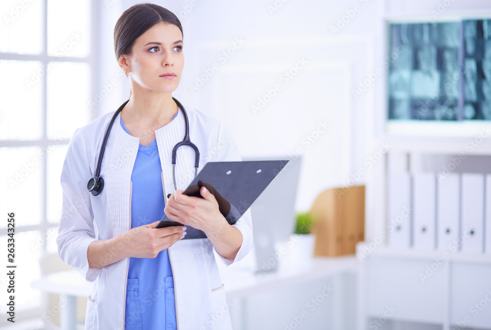 Young smiling female doctor with stethoscope holding a folder at a hospital's consulting room Young smiling female doctor with stethoscope holding a folder at a hospital's consulting room