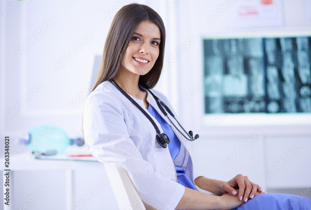 Beautiful female doctor sitting in a consulting room, smiling at the camera Beautiful female doctor sitting in a consulting room, smiling at the camera