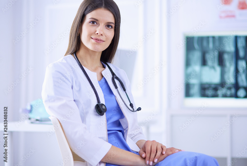 Beautiful female doctor sitting in a consulting room, smiling at the camera Beautiful female doctor sitting in a consulting room, smiling at the camera