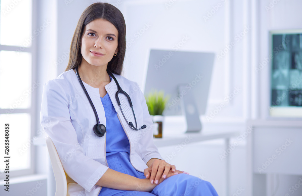 Beautiful female doctor sitting in a consulting room, smiling at the camera Beautiful female doctor sitting in a consulting room, smiling at the camera