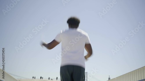 Rear view of African American sportsman skipping rope on bridge. Young man warming up before training. Concept of sport  photo