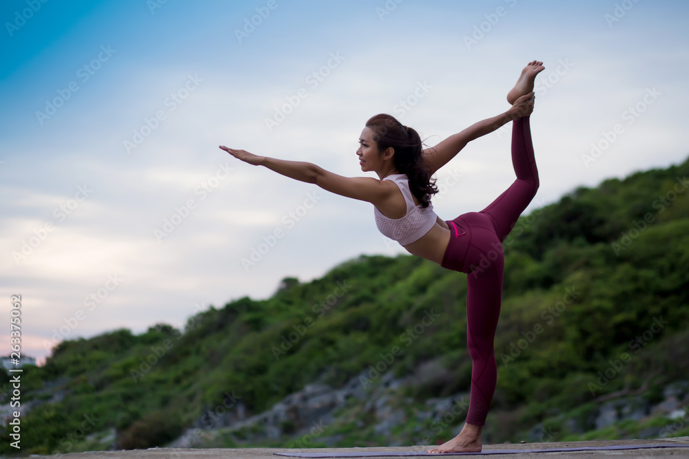 Side view of healthy happy women practicing yoga. standing stretching in Natarajasana pose, beautiful landscape view sky on evening nature evening outdoor, concept for exercising, health care