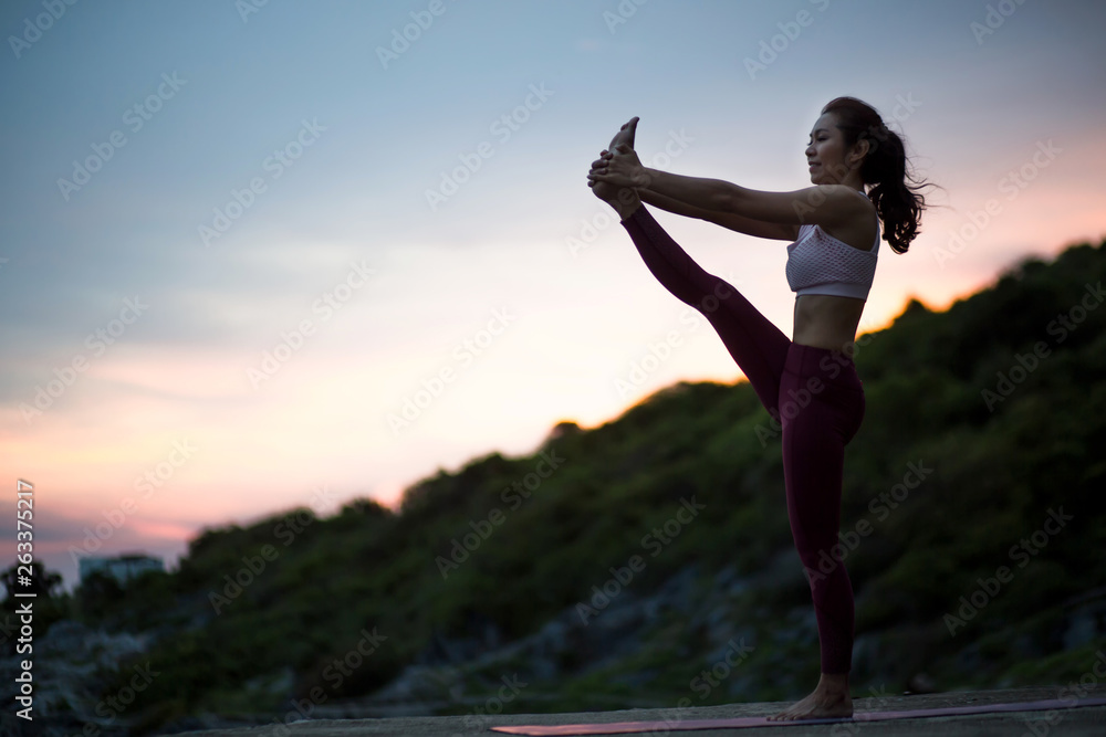 Side view of healthy women practicing yoga. standing Utthita Hasta Padangusthasana exercise, Extended Hand to Big Toe pose..beautiful landscape view sky on evening sunset nature evening outdoor.