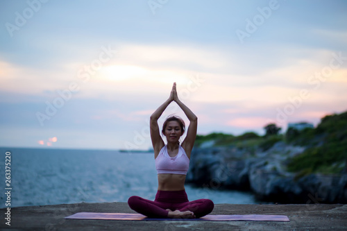 Young woman doing exercise yoga. sitting in Sukhasana exercise, Easy Seat pose pose. Amazing yoga landscape in beautiful sky and enjoying sea view with evening, concept for exercising, health care