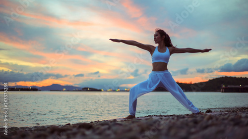 Healthy women practicing yoga. warrior ll pose on the beach at morning .Yoga virabhadrasana..landscape view sky on morning outdoor near sea, concept for exercising, healthcare. copy space