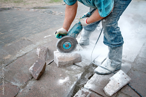 Worker saws stone with circular saw for repairing and renewal the walkway. Builder, work on laying paving slabs. Tiler cuts paving slub using electric cut-off saw