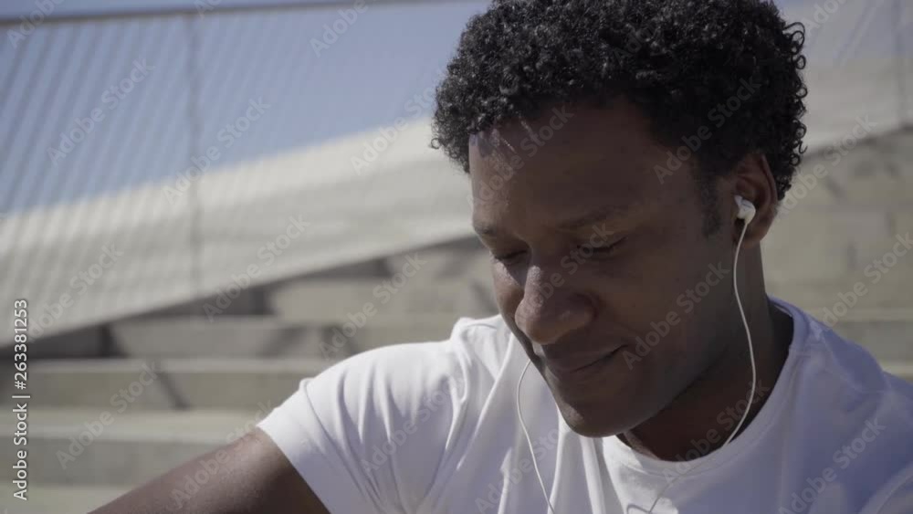 Closeup shot of African American man with earphones. Handsome smiling guy listening music outdoor. Technology concept Closeup shot of African American man with earphones. Handsome smiling guy listening music outdoor. Technology concept