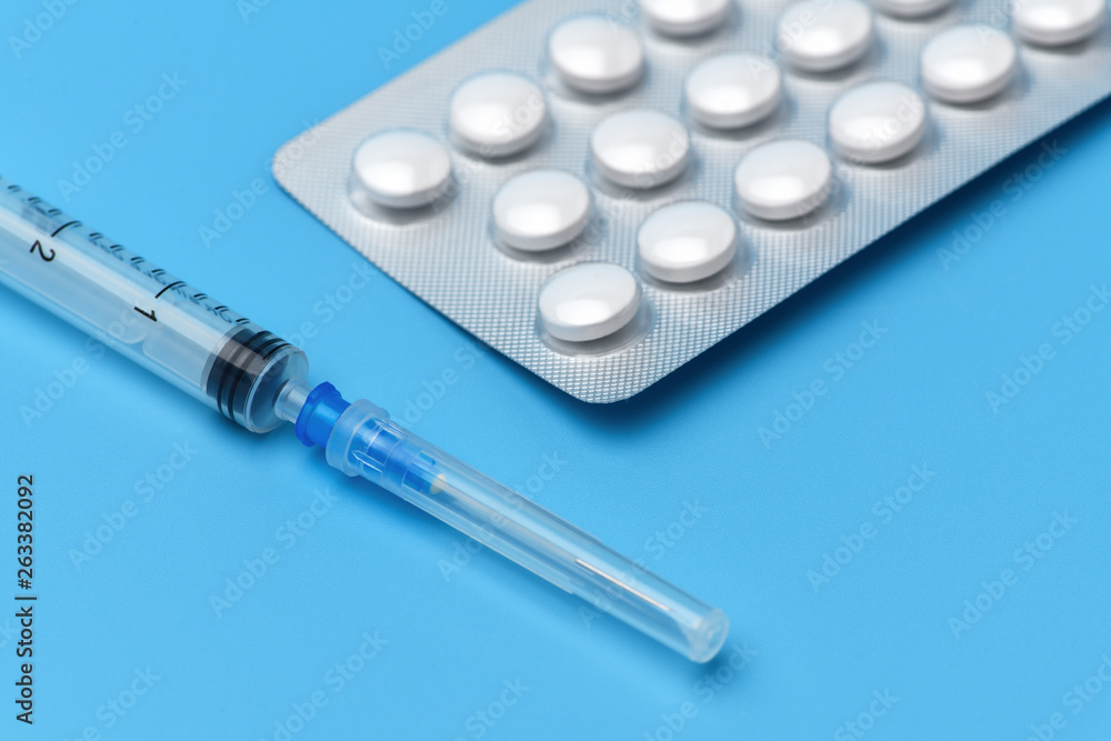 Many tablets are on a blue background, at the bottom is a syringe with an injection. Drugs and pills prescription background. Pharmaceutical preparation. Many tablets are on a blue background, at the bottom is a syringe with an injection. Drugs and pills prescription background. Pharmaceutical preparation.