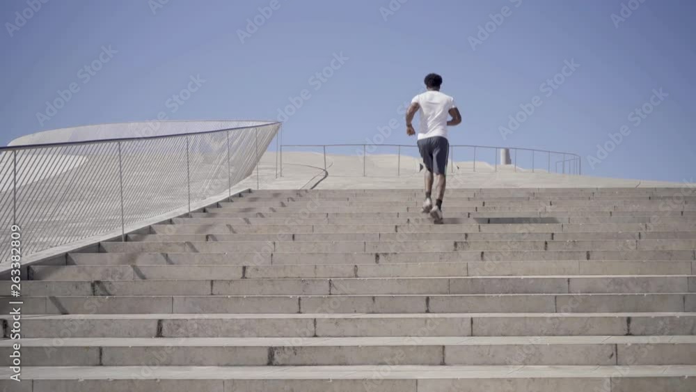 Rear view of African American man running upstairs. Young male runner training during sunny summer day. Concept of sport Rear view of African American man running upstairs. Young male runner training during sunny summer day. Concept of sport