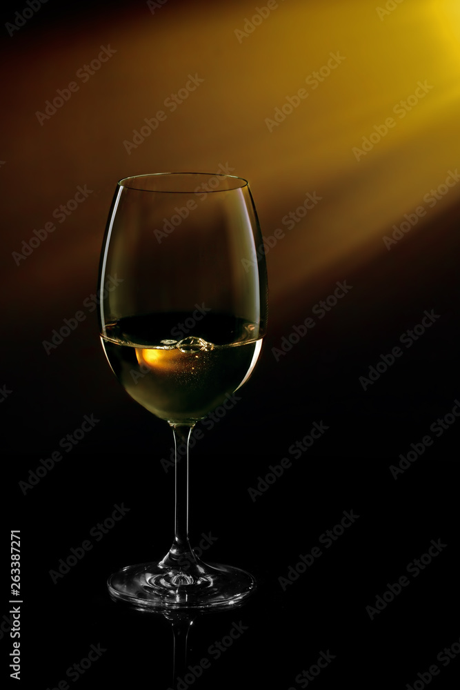 Glass of white wine on black to yellow background. Concept studio shot.