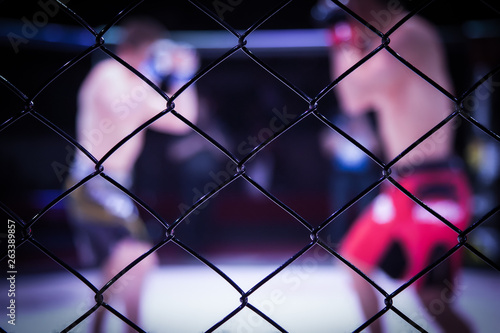 Sports concept of fighting without rules.Two boxer athletes in the arena of the octagonal scene.Mood boxing fights without boxing rules MMA. An alternative look at boxing fights through the metal cage