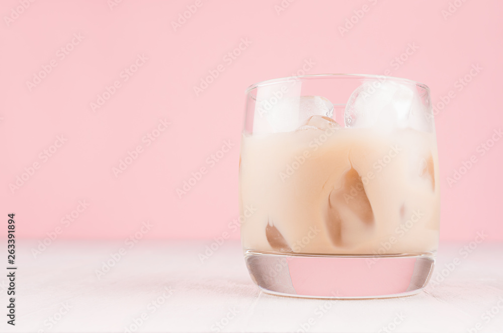 Baileys liqueur in misted glass with ice cubes closeup on pastel pink background and white wooden table, copy space. Baileys liqueur in misted glass with ice cubes closeup on pastel pink background and white wooden table, copy space.