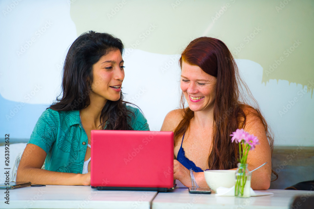 young happy and beautiful caucasian and latin women working at office cafe with laptop computer discussing as digital business partners and diversity ethnicity friends