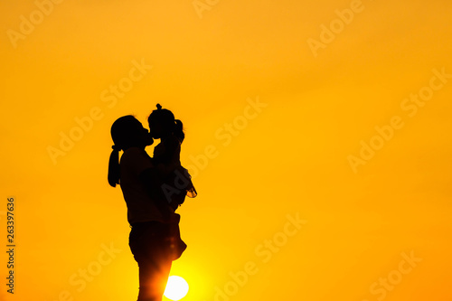 The family silhouette of the mother and child standing watch the sunset and the sky in orange in evening