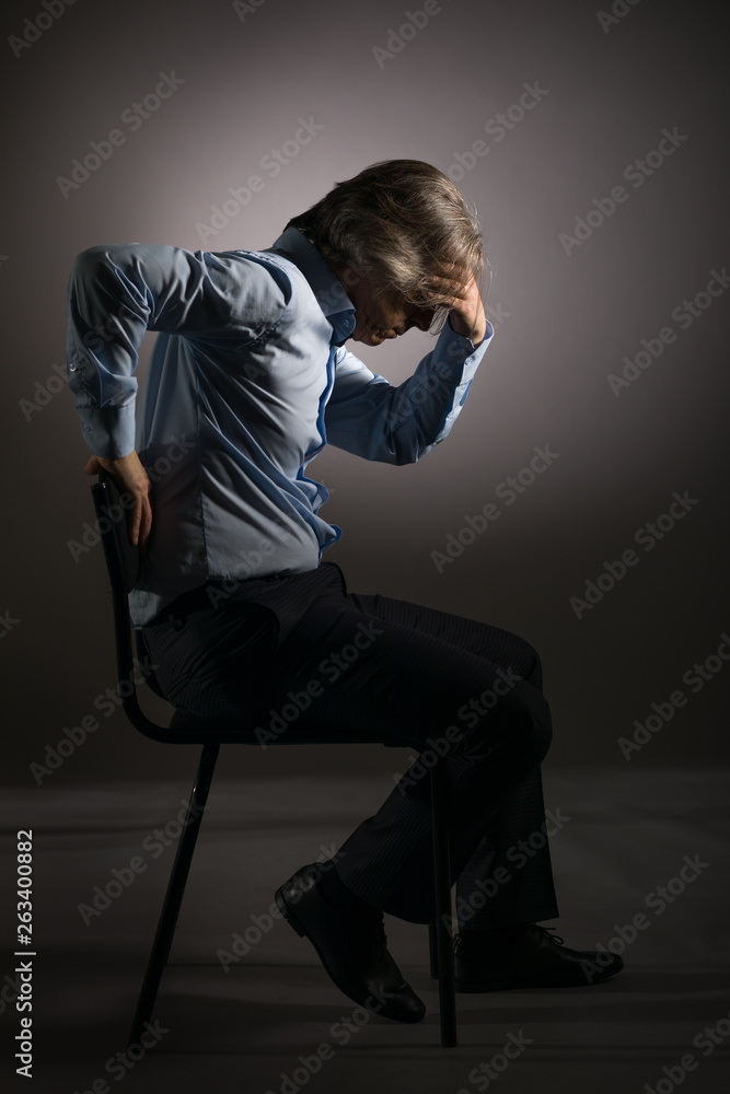 Businessman in a state of stress holding his head, sitting on a chair on a dark background. Businessman in a state of stress holding his head, sitting on a chair on a dark background.